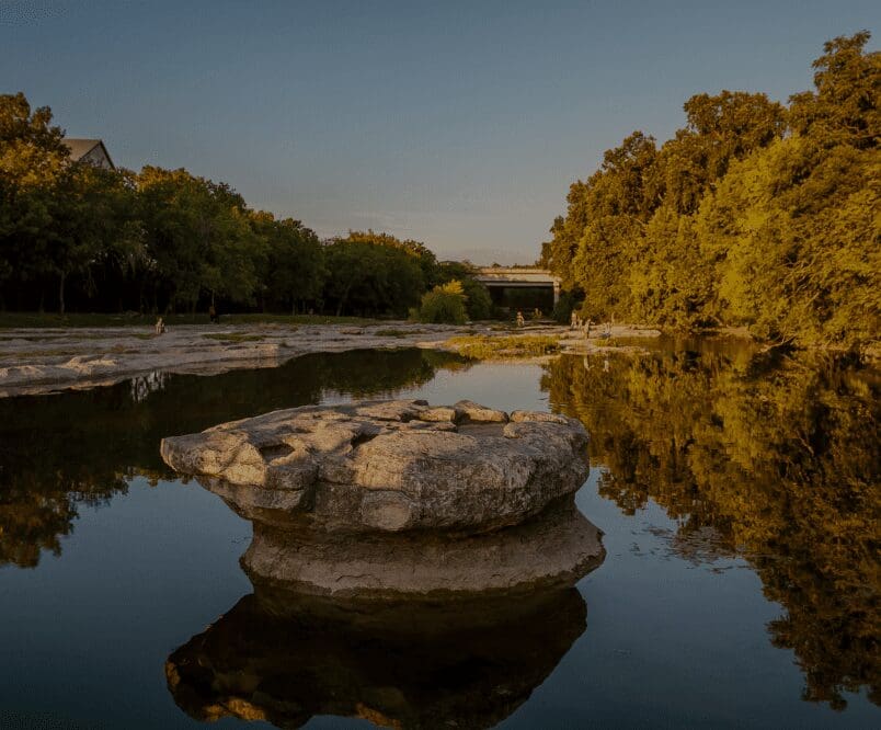 Rock in calm river surrounded by trees.